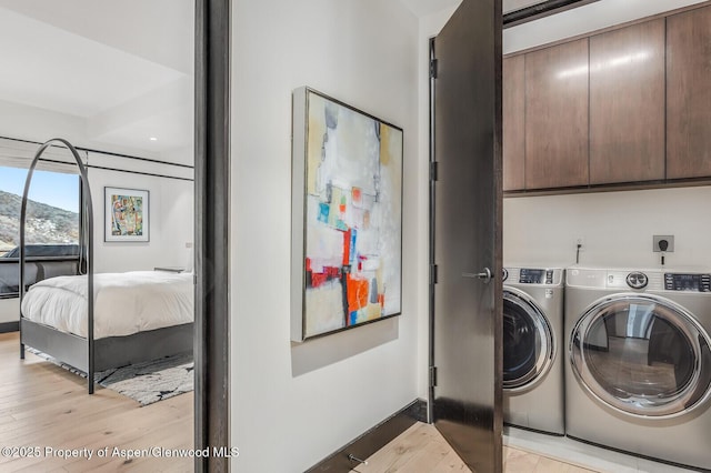 washroom featuring washer and dryer, cabinets, and light wood-type flooring