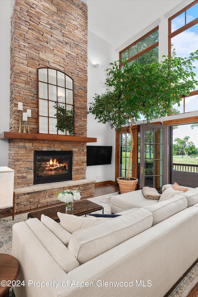 living room featuring a stone fireplace, a high ceiling, and wood-type flooring