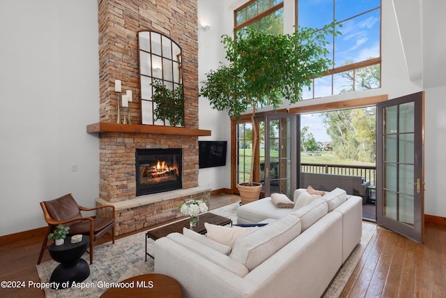 living room with hardwood / wood-style floors, a towering ceiling, a fireplace, and french doors