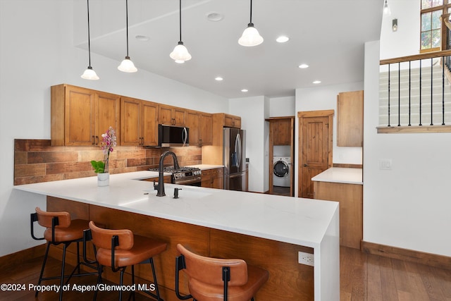 kitchen featuring kitchen peninsula, appliances with stainless steel finishes, backsplash, decorative light fixtures, and washer / dryer