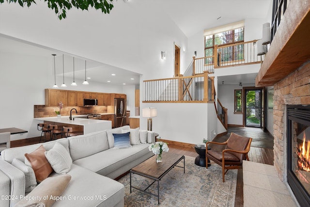 living room with sink, hardwood / wood-style floors, a towering ceiling, and a stone fireplace