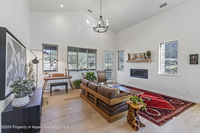 living room featuring a notable chandelier, light wood-type flooring, and high vaulted ceiling