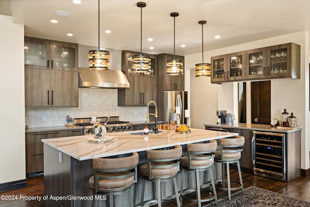 kitchen featuring stainless steel refrigerator with ice dispenser, light stone counters, beverage cooler, a kitchen island with sink, and hanging light fixtures