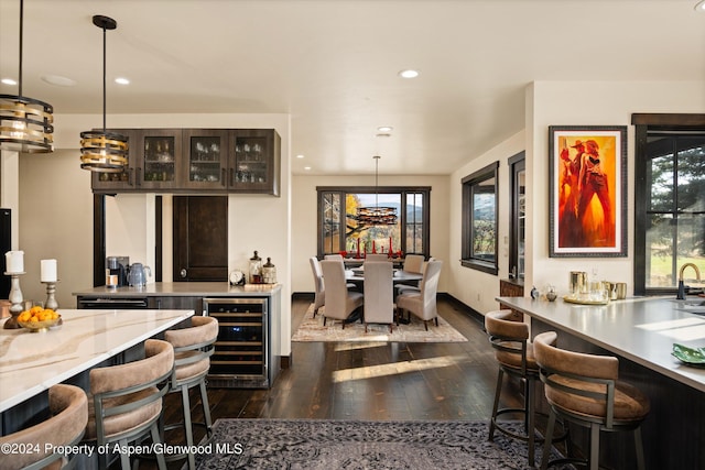 kitchen featuring hanging light fixtures, wine cooler, dark brown cabinets, dark hardwood / wood-style flooring, and a breakfast bar area