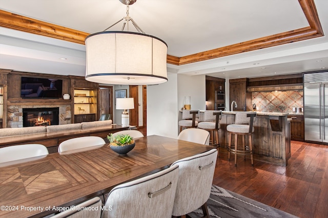 dining area with sink, dark wood-type flooring, a stone fireplace, built in features, and crown molding