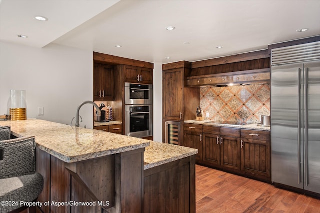 kitchen featuring wine cooler, light stone counters, decorative backsplash, and appliances with stainless steel finishes