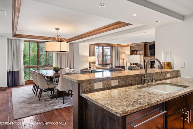 kitchen with sink, dark wood-type flooring, a raised ceiling, light stone counters, and dark brown cabinets