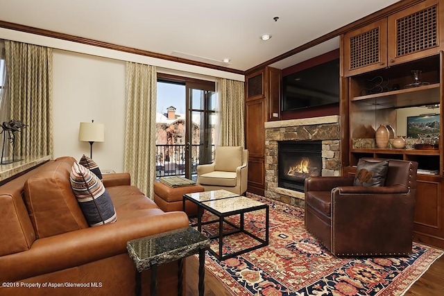 living area with a stone fireplace, ornamental molding, and wood finished floors