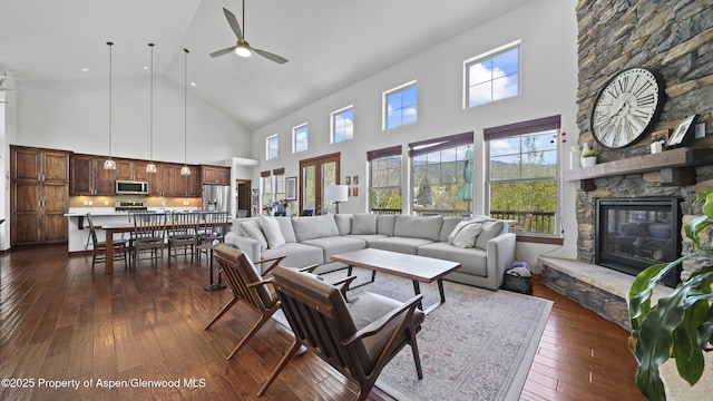 living room with a stone fireplace, dark wood-type flooring, and a high ceiling