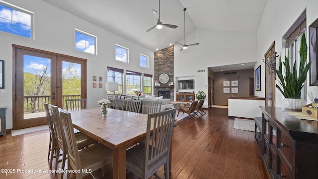 dining room with a stone fireplace, dark wood-type flooring, high vaulted ceiling, and french doors