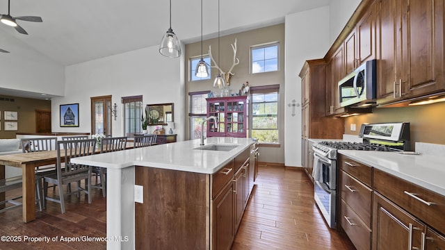 kitchen featuring sink, hanging light fixtures, ceiling fan, stainless steel appliances, and a kitchen island with sink