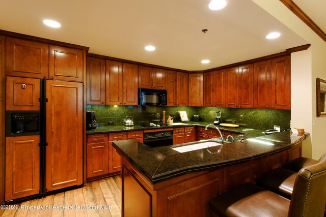 kitchen featuring kitchen peninsula, a kitchen breakfast bar, sink, black appliances, and dark stone countertops