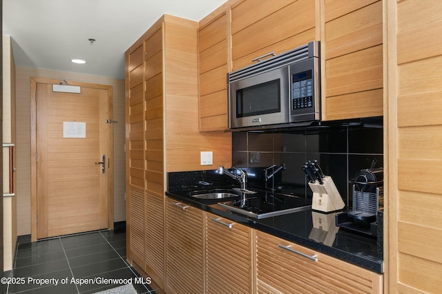 kitchen with dark tile patterned floors, a sink, stainless steel microwave, dark countertops, and decorative backsplash