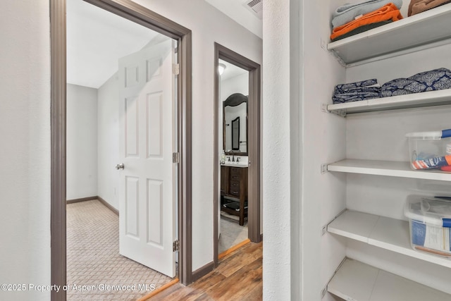 corridor with baseboards, visible vents, a sink, and light wood-style floors