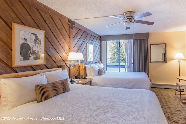 bedroom featuring wood walls, ceiling fan, baseboard heating, and a textured ceiling