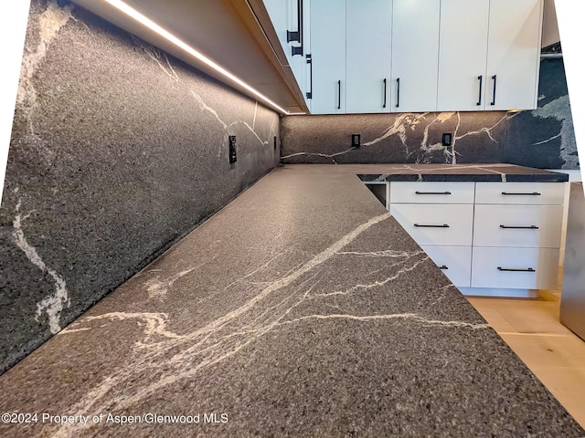 room details featuring white cabinets, tasteful backsplash, and dark stone countertops