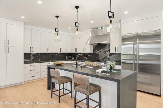 kitchen with sink, stainless steel appliances, extractor fan, decorative light fixtures, and a kitchen island with sink