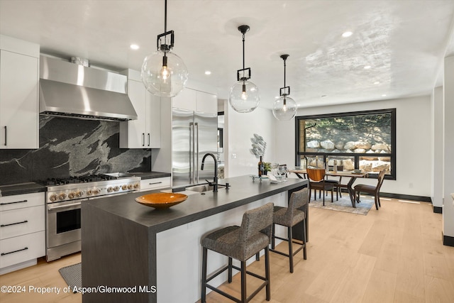 kitchen with wall chimney exhaust hood, premium appliances, white cabinetry, and a kitchen island with sink