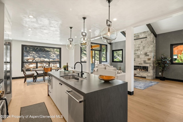 kitchen featuring a kitchen island with sink, sink, white cabinetry, a stone fireplace, and hanging light fixtures