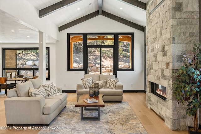 living room with lofted ceiling with beams, light hardwood / wood-style flooring, and a stone fireplace