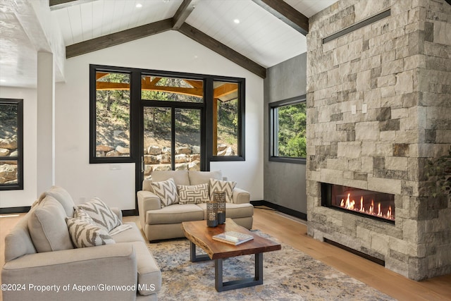 living room with lofted ceiling with beams, light hardwood / wood-style floors, and a stone fireplace