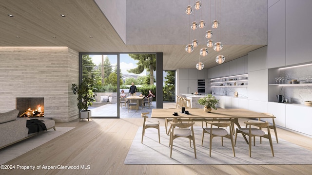 dining room with floor to ceiling windows, a towering ceiling, a fireplace, and light hardwood / wood-style flooring