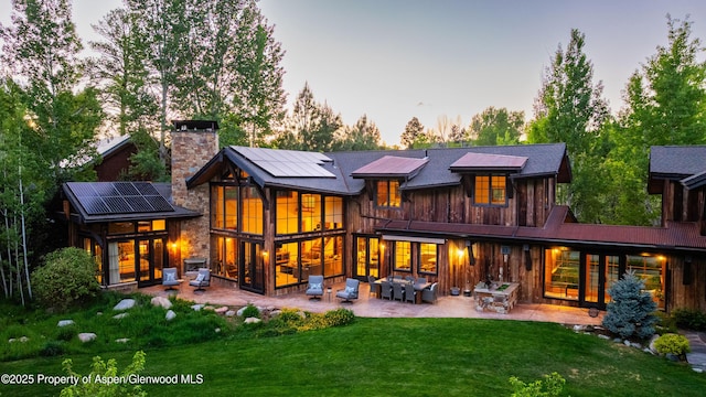 236 Bristlecone Dr, Carbondale, CO 81623 - back of house at dusk featuring a patio, a chimney, solar panels, a yard, and an outdoor hangout area