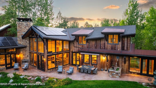 236 Bristlecone Dr, Carbondale, CO 81623 - back of property at dusk featuring solar panels, a patio area, a chimney, a sunroom, and board and batten siding