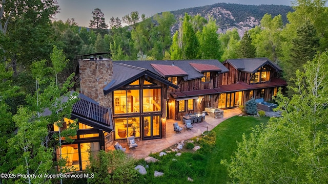 236 Bristlecone Dr, Carbondale, CO 81623 - back of property at dusk with a patio area, a chimney, a view of trees, and a mountain view