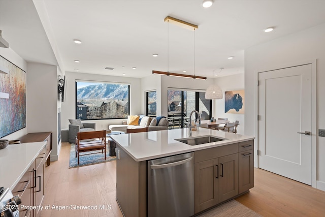 kitchen with a kitchen island with sink, a sink, light countertops, stainless steel dishwasher, and light wood-type flooring