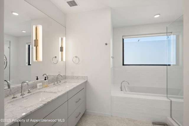 full bathroom featuring tiled bath, visible vents, double vanity, and a sink