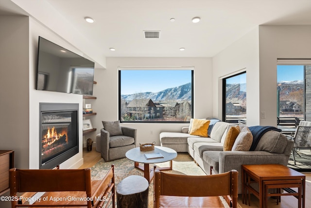 living area with a glass covered fireplace, recessed lighting, wood finished floors, and visible vents