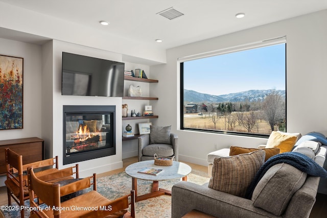 living area featuring visible vents, a glass covered fireplace, wood finished floors, recessed lighting, and baseboards