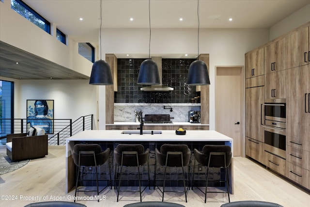 kitchen featuring pendant lighting, decorative backsplash, a kitchen island with sink, and a breakfast bar area