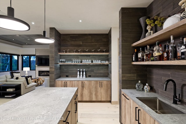 bar with a tile fireplace, light wood-type flooring, hanging light fixtures, and sink