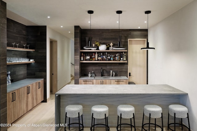 bar featuring decorative light fixtures, light hardwood / wood-style flooring, and sink