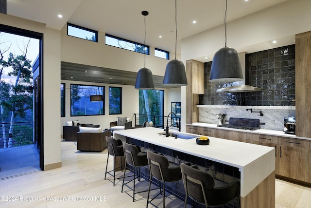 kitchen featuring a kitchen island with sink, black gas stovetop, wall chimney exhaust hood, tasteful backsplash, and decorative light fixtures