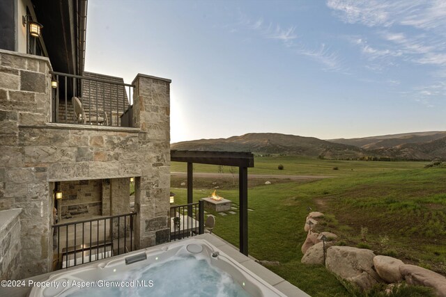 exterior space featuring a fireplace, a mountain view, a hot tub, and a rural view