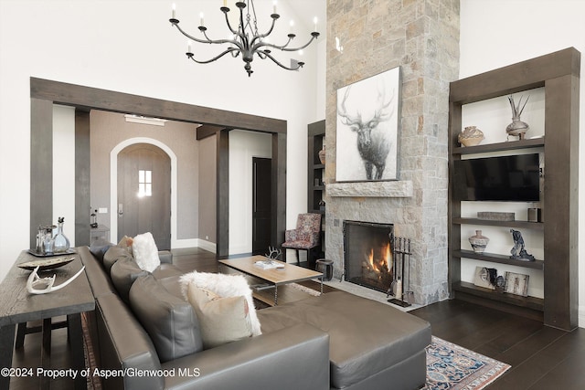 living room featuring arched walkways, a stone fireplace, a high ceiling, dark wood finished floors, and an inviting chandelier