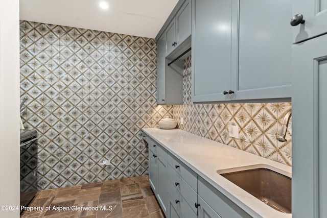 kitchen featuring decorative backsplash, stone finish flooring, gray cabinets, light countertops, and a sink