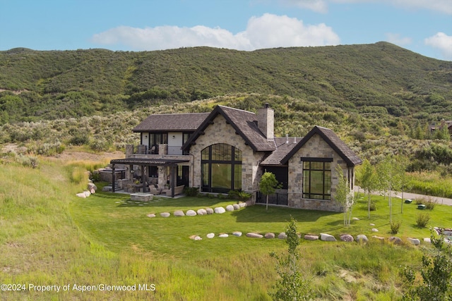 exterior space with stone siding, a mountain view, a chimney, and a front lawn