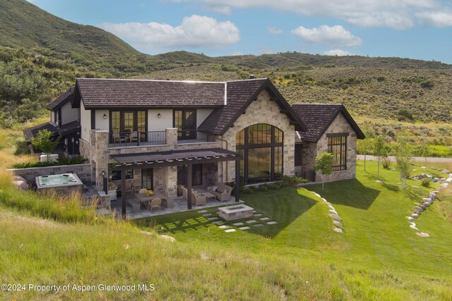 exterior space with a patio, a mountain view, a balcony, an outdoor hot tub, and stone siding