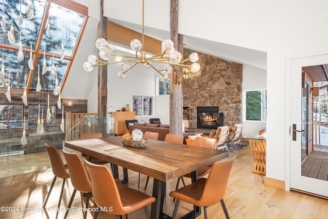 dining area featuring light hardwood / wood-style floors, a fireplace, high vaulted ceiling, and a chandelier