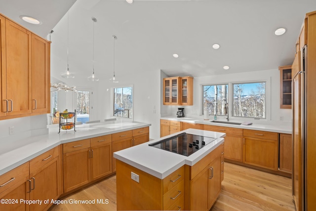 kitchen with black electric stovetop, light wood-type flooring, sink, a kitchen island, and hanging light fixtures