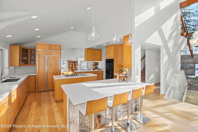 kitchen with a breakfast bar, black appliances, sink, hanging light fixtures, and a kitchen island