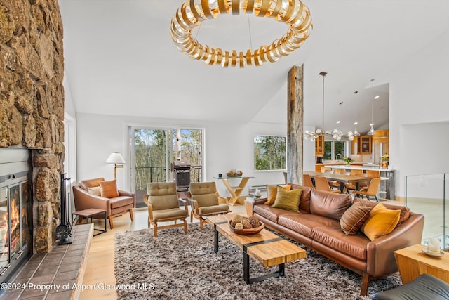 living room featuring a fireplace, high vaulted ceiling, a chandelier, and light hardwood / wood-style flooring