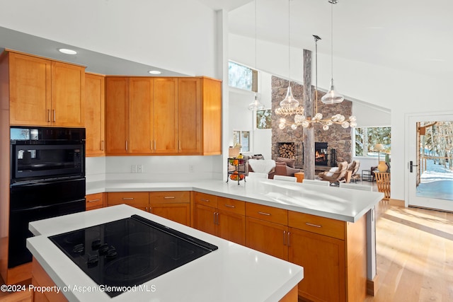 kitchen with kitchen peninsula, light wood-type flooring, electric cooktop, oven, and a stone fireplace