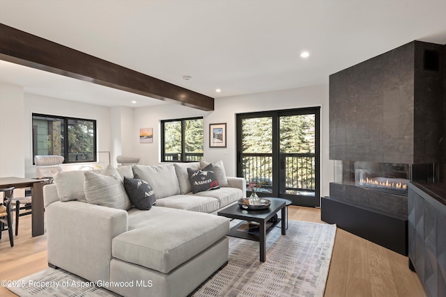 living room with beamed ceiling, a large fireplace, and light hardwood / wood-style flooring