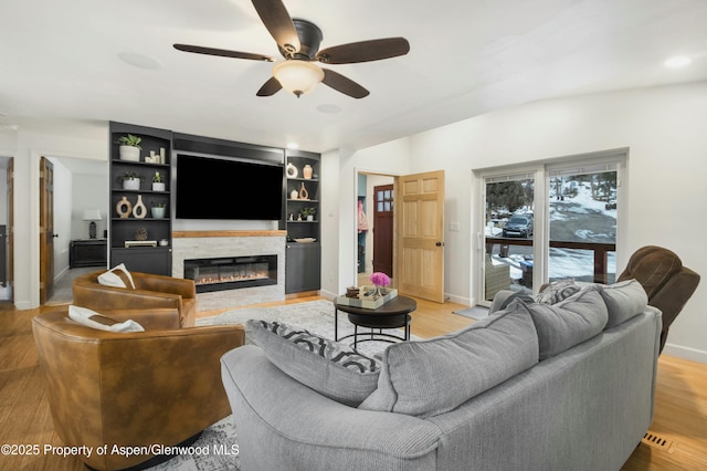 living room featuring ceiling fan, light wood-type flooring, built in shelves, and a fireplace