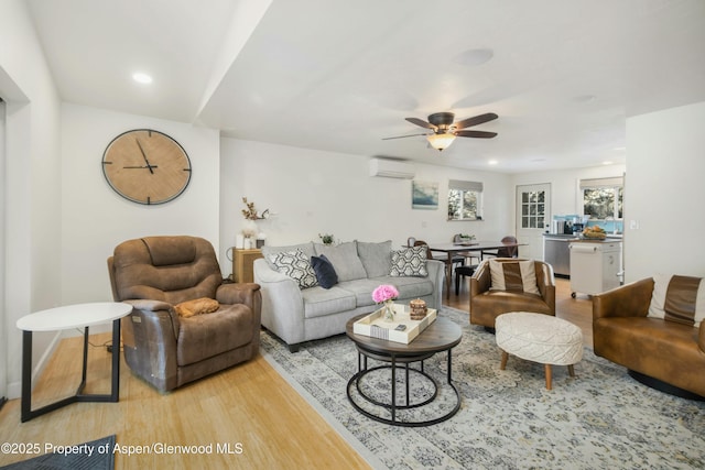 living room with ceiling fan, a wall mounted air conditioner, and light hardwood / wood-style flooring